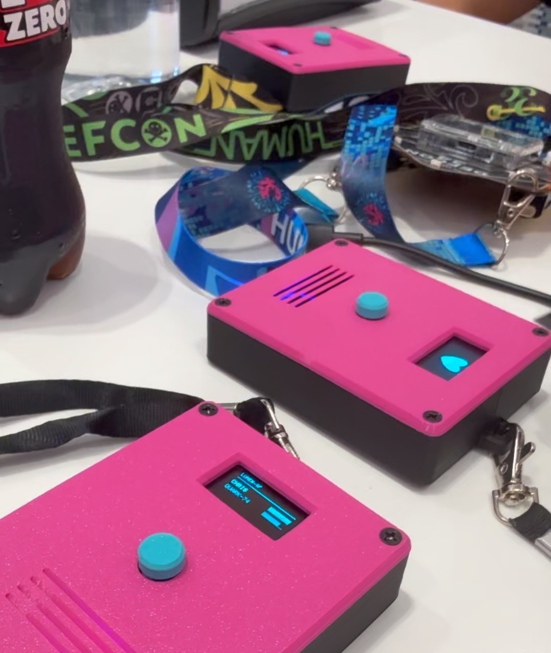 Three badges on a table at the con, one showing the crew roster with signal bars, one showing the heart screensaver